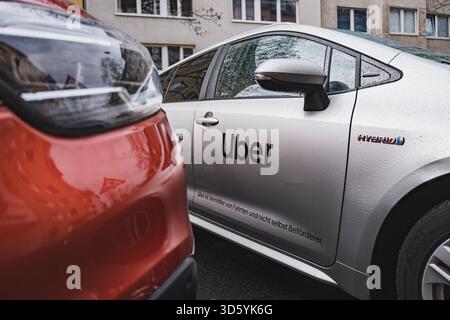 Auto ibrida Silver Uber parcheggiata in una strada cittadina vicino a un veicolo rosso Foto Stock