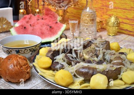 Tradizionale beshbarmak kazako con fette di anguria e decanter di vodka Foto Stock