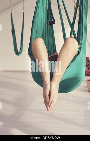 La persona maschile fa esercizio di lezioni di yoga sull'amaca. Meditazione in aria calma. Allenamento in studio per principianti Aero. Stile di vita degli uomini. Ragazzo che allena la posa zen. Verde. Amaca Foto Stock