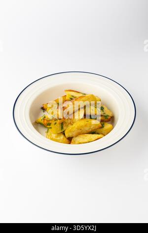 Patate arrostite dorate con erbe fresche in una ciotola su sfondo bianco Foto Stock