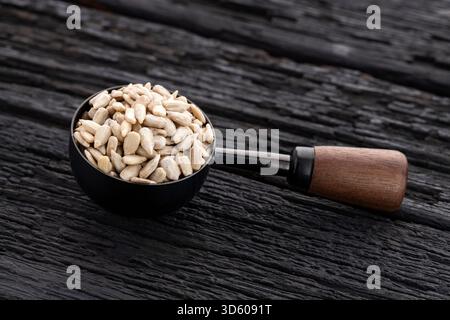 Semi di girasole sgusciati in un cucchiaio di metallo e legno - Helianthus annuus Foto Stock