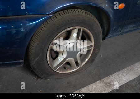 Primo piano di uno pneumatico sgonfio su una vecchia auto blu nel garage Foto Stock