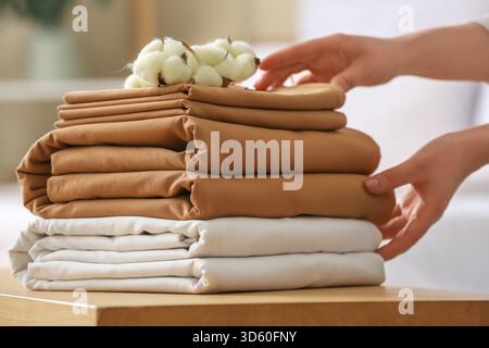 Mani femminili e pila di biancheria da letto con fiori di cotone sulla panca in camera da letto, primo piano Foto Stock