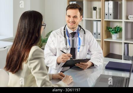 Sorridente giovane medico maschio parlare con paziente donna, dando consulenza durante la visita medica Foto Stock