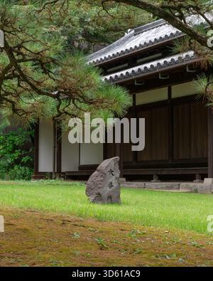 Una scena tranquilla caratterizzata da una tradizionale casa di guardia in legno e un cartello in pietra ricoperto di muschio con calligrafia kanji. Foto Stock