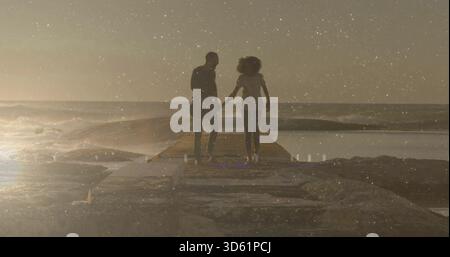 Coppia informale che cammina tenendo per mano il molo di cemento al tramonto con onde di chitarra che riflettono Foto Stock