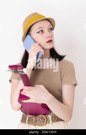 Giovane musicista che effettua una telefonata, tiene il dispositivo all'orecchio e ascolta con attenzione mentre guarda attentamente lontano. Bella donna giocatrice di ukulele Foto Stock