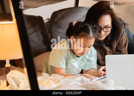Mamma asiatica con la sua giovane figlia carina stanno giocando sotto il tavolo. Una famiglia felice si diverte insieme. Messa a fuoco selettiva. Foto Stock