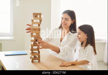 Madre e figlia sorridenti giocano a una partita di jenga a blocchi di legno, godendosi momenti di qualità insieme a casa. Foto Stock