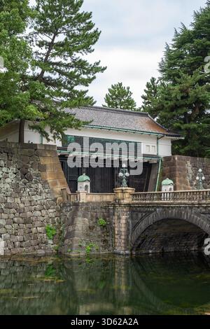 The historical stone Sakuradamon and bridge crossing the tranquil moat of the Imperial Palace grounds in Tokyo, framed by ancient pine trees. Foto Stock