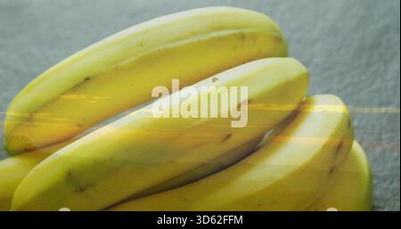 Telaio di riempimento, mazzo di banane gialle mature poggiate su un bancone grigio testurizzato che riflette la luce Foto Stock