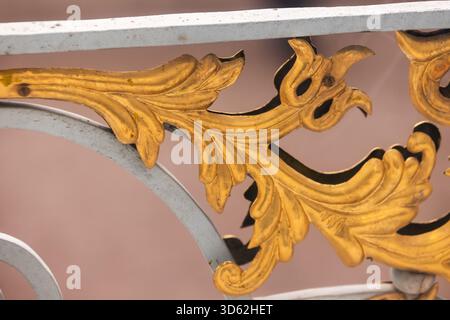 Primo piano di scrollwork in foglia oro dorata su una balaustra decorativa in metallo. Il design decorato evoca l'eleganza barocca, il lusso e la maestria artigianale, aggiungendo Foto Stock