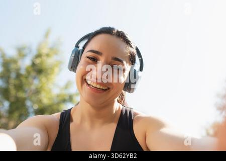 Una giovane donna scatta un selfie mentre ascolta musica e pratica sport in un parco la mattina, Saragozza, Spagna Foto Stock