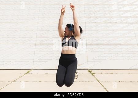 Una giovane donna salta e balla felice di rilassarsi e distendersi dopo una sessione sportiva all'aperto, in una giornata di sole Foto Stock