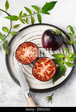 Pomodori "Bandol Blues" appena tagliati (Solanum lycopersicum) con buccia viola profonda e polpa rossa brillante su un piatto di ceramica. Foto Stock
