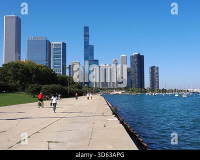 Chicago, USA - 15 settembre 2025: Persone che camminano e pedalano sul Lakefront Trail, con lo skyline di Chicago e il lago Michigan sullo sfondo. Foto Stock