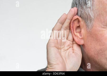 Uomo anziano con sintomo di perdita dell'udito, o persona sorda con gesto della mano per ascoltare Foto Stock