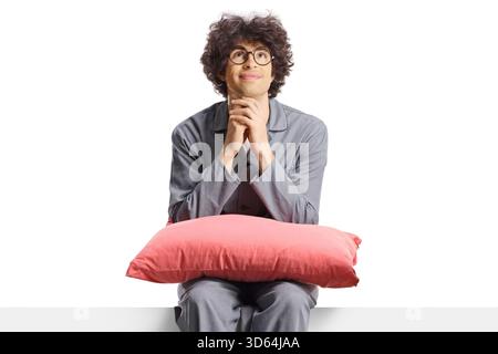 Giovane in pigiama seduto su un pannello vuoto con un cuscino isolato su sfondo bianco Foto Stock