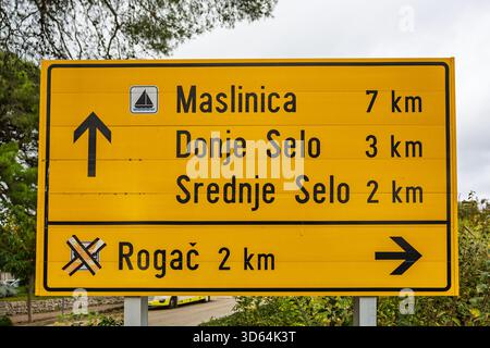 Un cartello stradale giallo brillante elenca le distanze da diverse città insulari croate, tra cui Stomorska, Donje Selo e Srednje Selo. La scena suggerisce trave Foto Stock