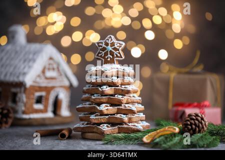 Albero di Natale fatto di biscotti al pan di zenzero, cannella, fetta di arancia secca e rami di abete su un tavolo grigio contro luci sfocate, primo piano Foto Stock