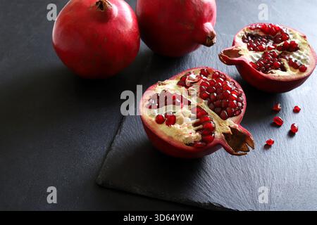 Melograno maturo fresco con taglio a metà e due melograno interi isolati su sfondo nero. Stile di vita sano. Vista dall'alto. Foto Stock