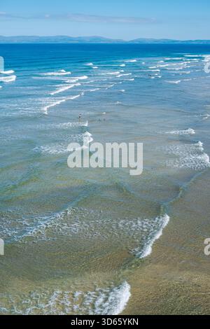 Le onde si infrangono dolcemente contro la costa sabbiosa di Finner Beach, mostrando le limpide acque turchesi sotto un cielo blu brillante. Un'atmosfera tranquilla inv Foto Stock