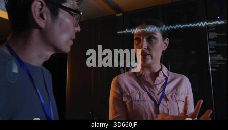 Donna che esegue gesti in camicia con badge blu che spiega i server nel data center, sovrapposizione delle forme d'onda Foto Stock