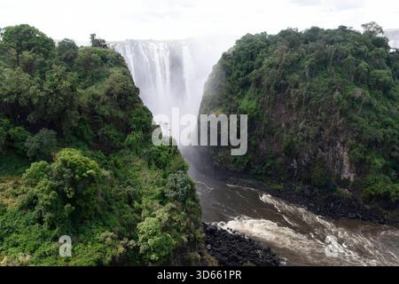 Blick auf einen Aussichtspunkt im Park Victoria Falls auf die Victoria Fälle, Die sich im Hintergrund befinden. während die linke Seite zu Simbabwe gehört, ist die rechte seite Staatsgebiet von Sambia. BEI den Victoriafällen donnert das Wasser des Sambesi auf einer Breite von 1,700 m Breite 110 m tief in eine 50 m Breite Schlucht. In der Regenzeit cadde hier bis zu 5,000 Kubikmeter Wasser pro minuto in Die Schlucht. DAS foto ist von der Victoria Fall Brücke aufgenommen, Die Simbabwe mit Sambia verbindet. Auf der linken Seite liegt Simbabwe und auf der rechten Sambia. Länge des Sambesi: 2,660 Foto Stock