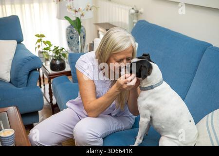 In un soggiorno soleggiato, si apre un momento di gioia mentre una donna interagisce dolcemente con il suo cane giocoso. I colori tenui e la luce brillante creano un'atmosfera calda Foto Stock