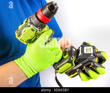 Foto isolata di mani maschili in guanti protettivi che trattengono un avvitatore a batteria e sostituiscono la batteria dell'accumulatore su sfondo bianco. Foto Stock