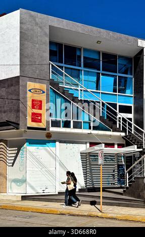 Moderno edificio commerciale con facciata in vetro e scalinata esterna nelle giornate di sole con due persone che camminano sul marciapiede Foto Stock