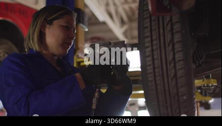 Utilizzo di tute blu e guanti neri da meccanico femminile con chiave pneumatica sulle ruote in garage Foto Stock