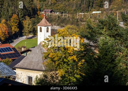 La fotografia cattura una vista panoramica di un villaggio, probabilmente nelle Alpi austriache, durante la stagione autunnale. Una piccola chiesa con un distintivo Foto Stock