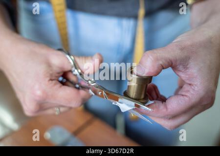 Mani che utilizzano forbici in metallo per tagliare il tessuto bianco da una bobina in ottone per la sartoria Foto Stock