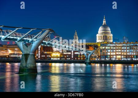 Al calare della sera, il Millenium Bridge attraversa elegantemente il Tamigi, mostrando splendidi riflessi mentre la cattedrale di St. Paul si erge maestosamente illuminata sullo sfondo. Foto Stock