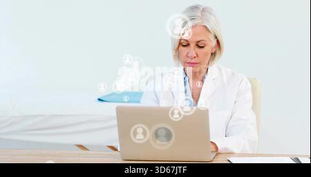 Digitando donna anziana in bianco cappotto medico immettendo record su laptop argento in clinica, icone avatar Foto Stock