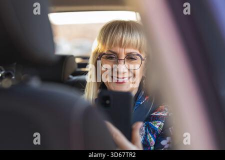 Donna anziana seduta sul sedile posteriore con smartphone Foto Stock