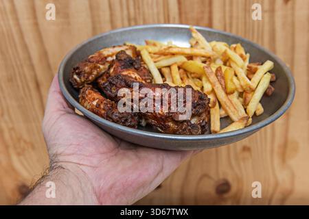 Pollo fritto croccante in stile meridionale con spicchi di patate al forno al rosmarino e aglio, servito su una tavola rustica di legno con salsa barbecue fatta in casa Foto Stock