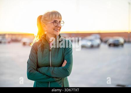 Ritratto di una donna anziana sorridente in abbigliamento sportivo in piedi in un parcheggio Foto Stock