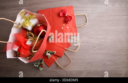 Concetto di acquisto di regali e decorazioni natalizie con sacchetti di carta rossa su un tavolo di legno. Vista dall'alto. Foto Stock