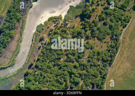 Foto aerea dall'alto verso il basso che mostra un ampio, asciutto e tortuoso letto di terra pallida, contrastando nettamente con la fitta foresta e i campi verdi. Rappresenta l'impatto visibile della grave siccità e del cambiamento climatico. Foto Stock