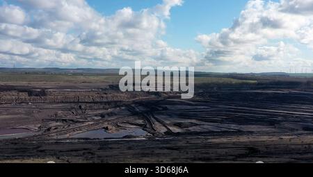 Prospettiva aerea di una grande miniera di lignite a cielo aperto che mostra il movimento terra su scala industriale e l'estrazione delle risorse, con turbine eoliche in lontananza Foto Stock