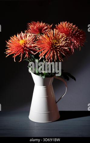 fiore di bronzo al crisantemo in brocca metallica su sfondo scuro Foto Stock