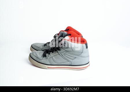 Un paio di sneaker alte usate in tela grigia con lacci neri slegati e dettagli rossi. Studio sparato, isolato sul bianco, nessuna gente Foto Stock
