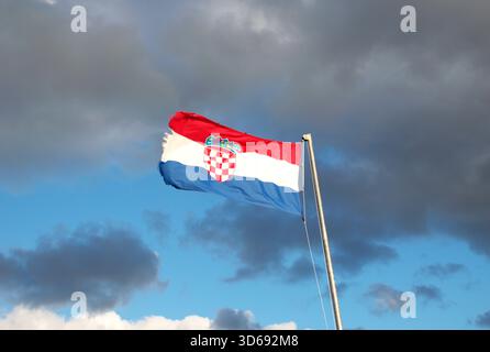 Vibrante bandiera croata con stemma che ondeggia in forte vento sotto un cielo nuvoloso. Patriottismo, identità nazionale, Europa, viaggi. Foto Stock