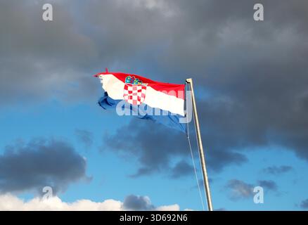 Vibrante bandiera croata con stemma che ondeggia in forte vento sotto un cielo nuvoloso. Patriottismo, identità nazionale, Europa, viaggi. Foto Stock