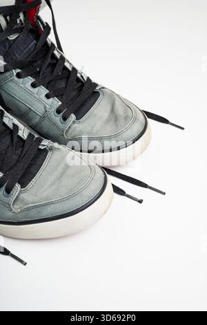 Un paio di sneaker alte usate in tela grigia con lacci neri slegati e dettagli rossi. Studio sparato, isolato sul bianco, nessuna gente Foto Stock