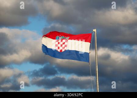 Vibrante bandiera croata con stemma che ondeggia in forte vento sotto un cielo nuvoloso. Patriottismo, identità nazionale, Europa, viaggi. Foto Stock