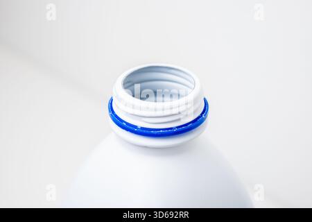Vista dall'alto verso il basso di una bottiglia di plastica bianca opaca vuota, generica, con un anello di sicurezza blu intorno all'apertura del collo. Ripresa in studio, isolata su bianco Foto Stock