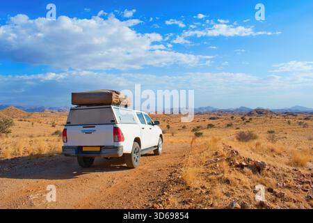 Auto fuoristrada con tenda sul tetto nel mezzo del paesaggio namibiano. Viaggio in Namibia. Foto Stock